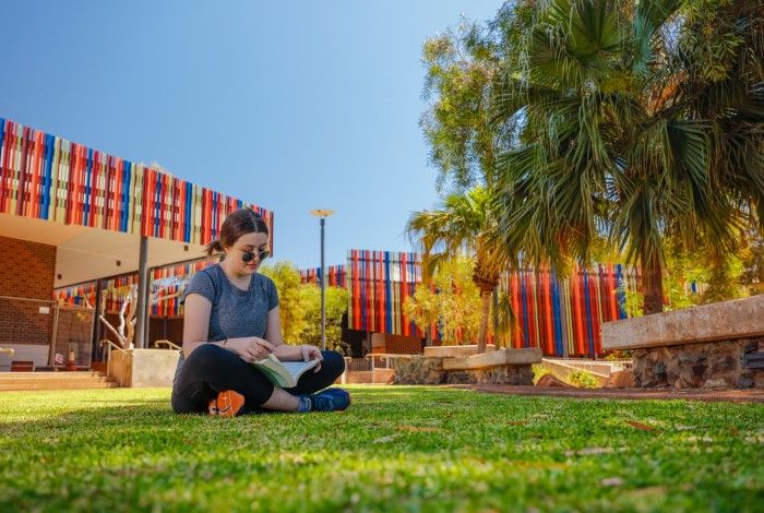 lady sitting on grass outside in front of Dampier library reading a book