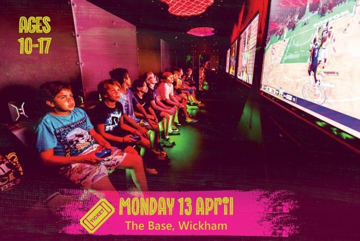 A group of young people sit in a gaming room playing video games on large screens, each holding controllers and focused on the gameplay. A pink banner reads “Monday 13 April – The Base, Wickham,” and text on the left says “Ages 10–17.”