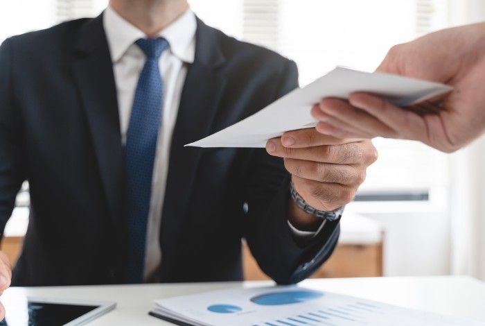 A businessman in a suit handing over a document to another person in an office setting, symbolising professional collaboration.
